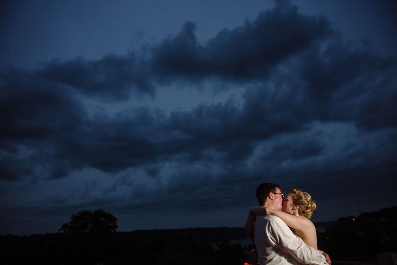 bride and groom kiss at night with clouds behind them