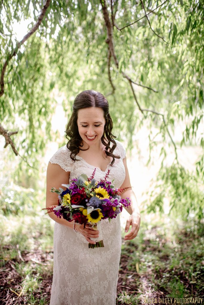 bride under willow trees looking at bouquet mn arboretum wedding