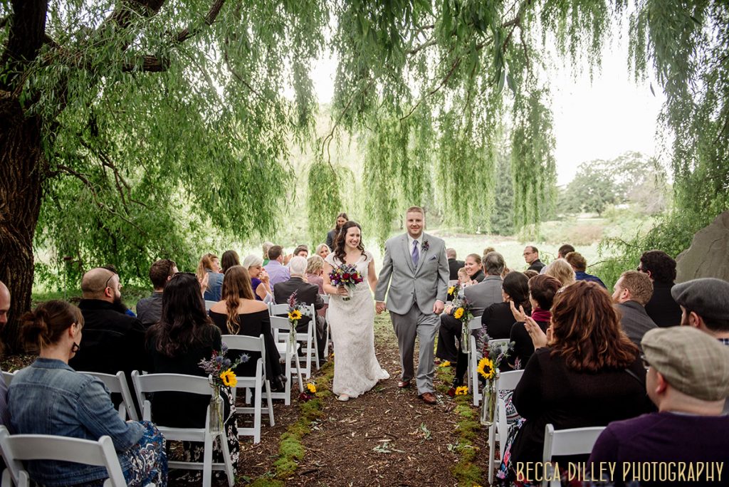 Couple recessional down aisle under willow trees mn arboretum wedding