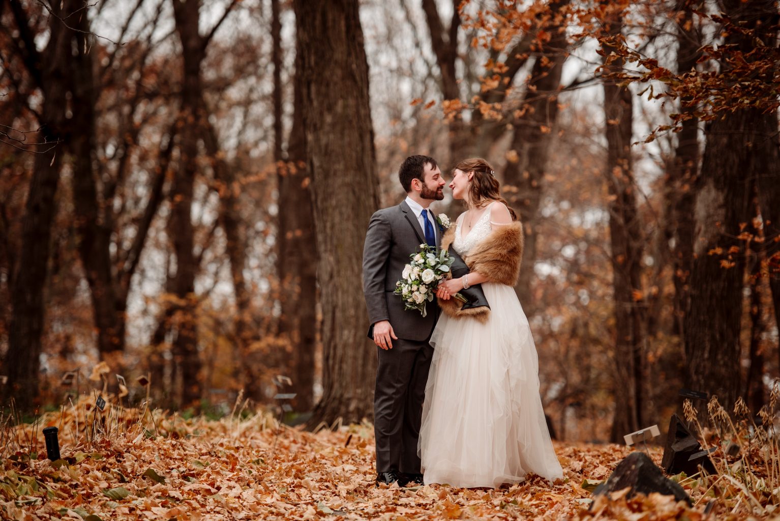 couple kiss under fall leaves in woods of mn arboretum 