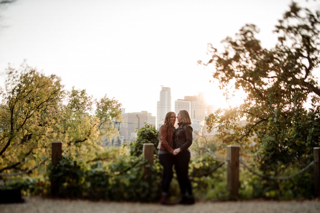 minneapolis skyline peeks through trees behind two brides as they embrace