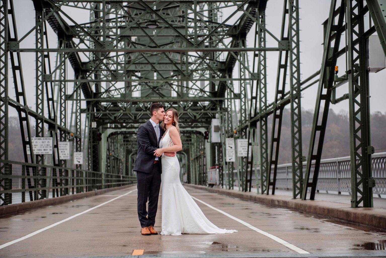 MN Stillwater liftbridge with newly married couple kissing in the middle of the bridge surrounded by green iron pillars
