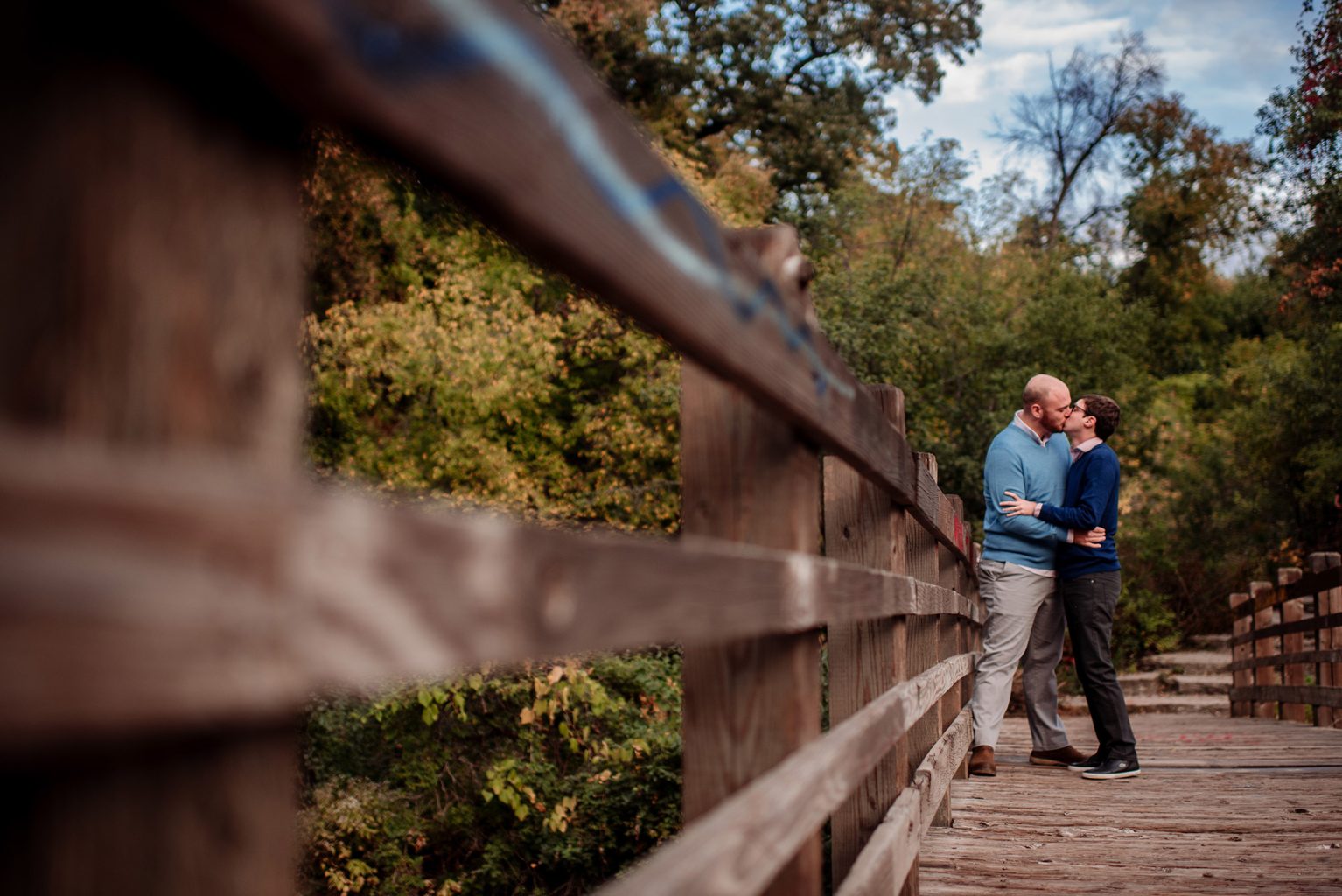 two grooms pose by bridge for engagement session minneapolis